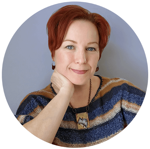 Photo of Dawn Sword, a woman with short red hair, semi-smile and chin resting on her hand. She's wearing a blue and tan striped sweater and a funky statement necklace..
