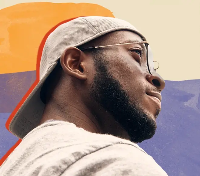 Black man with beard, glasses and backwards baseball cap looks into distance with hopeful strength